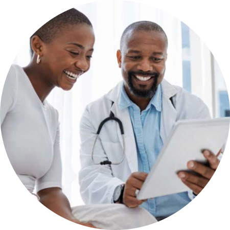 ForProvidersAssets_Photo1 A smiling doctor shows a tablet to a cheerful patient. Both appear engaged and happy during the consultation. The doctor is wearing a white coat and stethoscope.