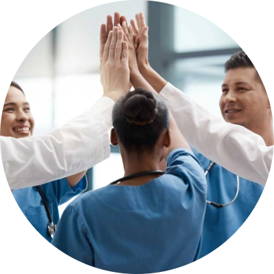 Partner_Photo2 Four healthcare professionals in scrubs and lab coats stand in a circle, smiling and giving a group high-five, celebrating teamwork in a bright, modern setting.
